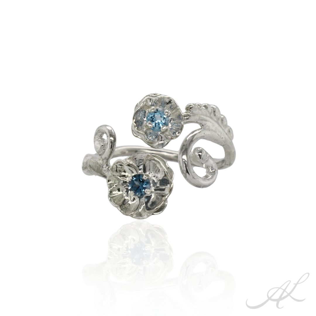 Silver floral poppy ring with blue gemstones on a white background